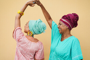 Happy african mother and daughter dancing while wearing traditional dresses - Mother day concept - Focus on senior face