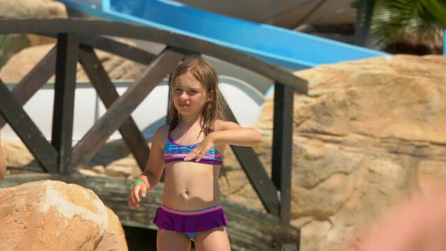 Cute girl in the swimsuit is dancing standing on the rocks on the pool