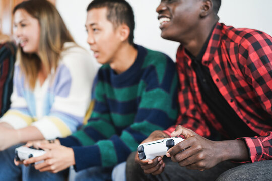 Multiracial young friends having fun playing video games at home - Focus on african boy hand