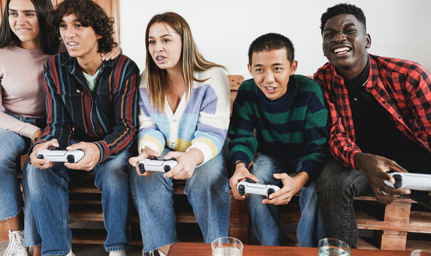 Multiracial young friends having fun playing video games at home - Focus on asian boy face