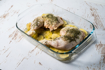 Two chicken thighs in a baking tray with potatoes, oregano and cava. Chicken breast with cava