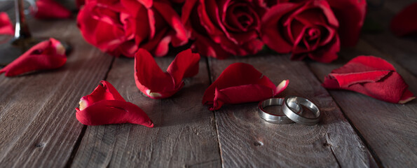Horizontal valentine's day vintage background with red roses and silver rings on rustic wooden...