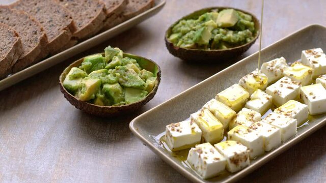 Pouring olive oil on spiced feta cheese cubes snack. Served with chunky guacamole and bread.