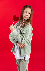 portrait of a beautiful girl in a green denim jacket and white shirt with loose hair. on a red background. close-up. heart on a stick. Valentine's Day. red candy