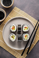 Sushi on round plate with chopsticks, soy sauce. ginger. Homemade rolls with salmon, avocado and cucumber.