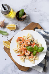 Mediterranean cuisine, seafood diet. Italian farfalle pasta with prawns garlic, basil and lemon on a marble tabletop. Top view flat lay.