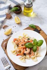 Mediterranean cuisine, seafood diet. Italian farfalle pasta with prawns garlic, basil and lemon on a marble tabletop.