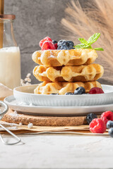 Traditional Belgian waffles stacked with fresh raspberries and blueberries sprinkled with powdered sugar on the kitchen counter