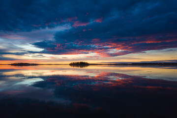 Magnificent sunrise over lake Malaren in Sweden, Calm water reflecting sky with dramatic clouds illuminated pink by sun, Orange yellow horizon with dark silhouette of islands, Scandinavia winter light