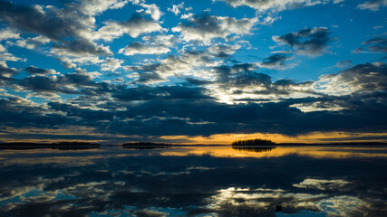 Naklejka na ściany i meble Morning light reflection in lake Malaren in Sweden, Sky reflected in calm water dramatic clouds, Golden horizon with dark silhouette of islands, Scandinavia winter gorgeous sunrise