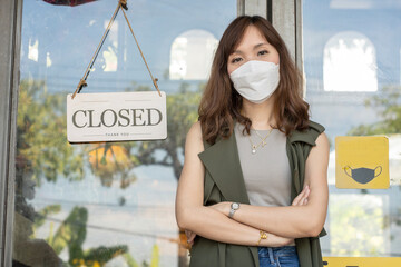 Asian woman who runs a restaurant business and wears a protective mask stands confidently with her...