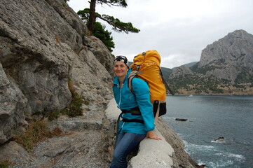 Young woman with a backpack is resting on a mountain trail along the sea.