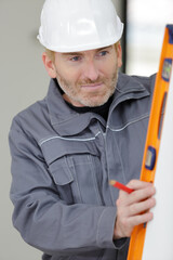 repairman in helmet is measuring wall with level