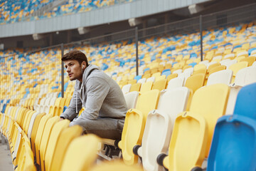Sportsman sitting on seat on stadium in earphones