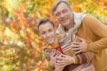 Fototapeta premium Portrait of smiling father and son hugging in autumn park