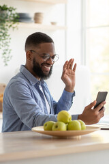 Happy young handsome african american businessman with beard in glasses waving hand at smartphone