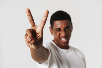 Young black man grimacing while showing peace sign