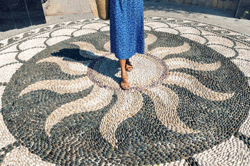 Woman walking on a beautiful mosaic on the pavement floor with decorative pattern of small stones...