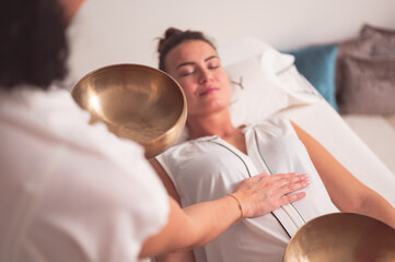 Female therapist with singing bowl practicing sound healing therapy on young woman