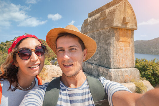 A man and a woman friends take a selfie against the background of the tomb while traveling along the Lycian way or trail.