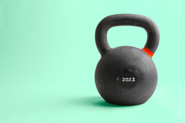 Naklejka na ściany i meble Horizontal studio shot of heavy black kettlebell with number 2022 on it, isolated on green background. Concept for new year resolutions, difficult year 2022 ahead.