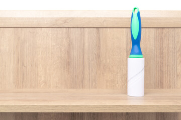 Adhesive pet hair remover roller standing vertical on a wooden board. Green and blue color of the handle.