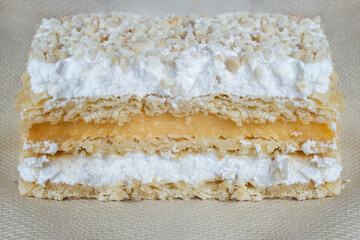 Close-up detail of crunchy overlapping layers of puff pastry millefeuille, filled with cream and meringue, and covered with chopped and au gratin almonds on a texture background. Traditional desserts.