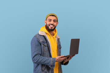 Freelance career. Happy arab guy using laptop computer and smiling to camera, posing over blue studio background