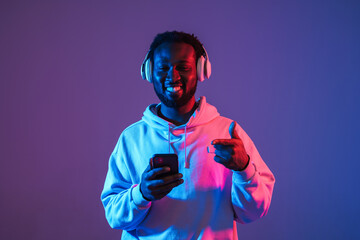 Black man in headphones using cellphone and pointing finger away