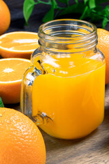 Fresh orange juice in a glass on a wooden background. Fresh Orange fruits with green leaves. Healthy vegan food. Vitamins food.Ripe oranges.Flat lay. Vertical orientation.