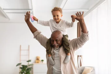 Foto op Canvas Cheerful Black Grandpa Carrying Little Grandson On Shoulders Playing Indoor © Prostock-studio
