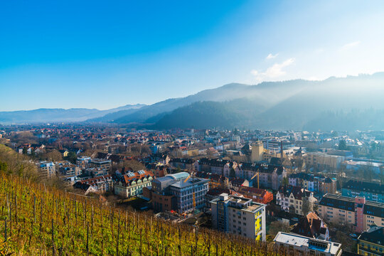 Germany, Freiburg im Breisgau city houses in valley between majestic black forest mountains schauinsland with sunrays and snow on cold winter day