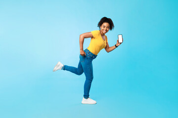 Huge online sale. Full length of happy young black woman with blank smartphone running on blue studio background, mockup