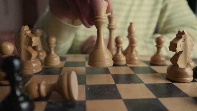 Senior chessplayer making move with white queen chess piece on wooden chessboard. Strategy of win and victory.