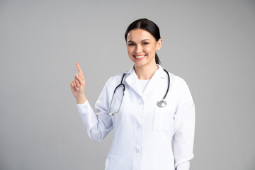 Waist up portrait view of the smiling happy doctor pointing with her finger at the free space on...