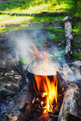 Tourist bowler with food on bonfire, cooking in the hike