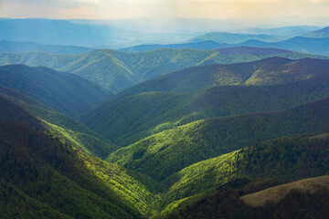 Fototapeta premium Misty haze on the hills. Colored sunrise in mountain slope. Sky with rain clouds. Beauty of nature concept background
