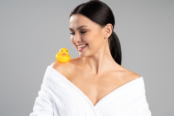 Obraz na płótnie Canvas Charming lady posing at the studio with a rubber duck after shower. Photo of lady after bath isolated on grey background. Skin care and beauty concept
