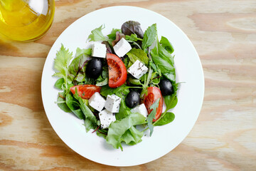 Fresh Greek salad in white plate at wooden table background. Closeup top view.
