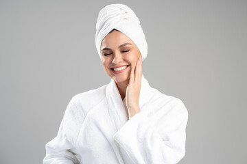Portrait view of the happy friendly young woman in white bath robe posing with closed eyes isolated on grey background with copy space. Portrait of female after body treatment