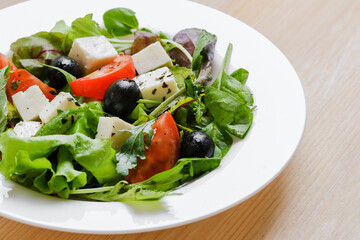 Fresh Greek salad in white plate at wooden table background. Closeup top view.