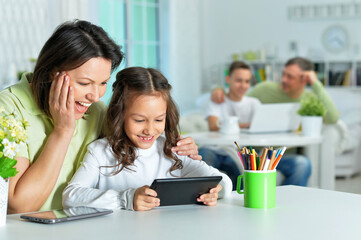 Portrait of smiling mother and daughter sitting at table and using digital tablet