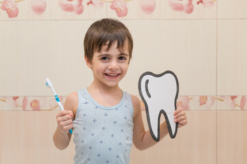 A little boy is holding a toothbrush and a paper tooth. Oral hygiene. The concept of a healthy lifestyle.