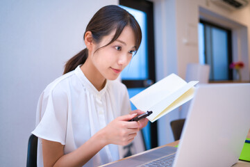 手帳を見ながらノートパソコンの画面を見る女性