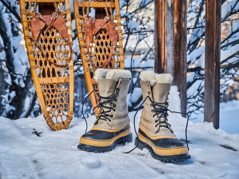 Heavy snow boots and classic wooden snowshoes on wooden deck in a backyard covered by snow