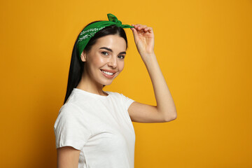 Young woman wearing stylish bandana on orange background, space for text