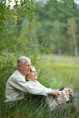 Naklejka na ściany i meble Portrait of happy senior couple sitting by pond