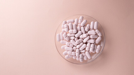 Oval pills in round plate on pink background with copy space. Creative concept for Valentine's Day or Pharmacy, Dietary Supplement and Medicines. Horizontal.