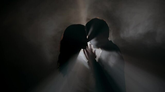 Silhouette of a couple in the dark 4K. Mystical atmosphere, smoke, spotlight. Man and woman in the night