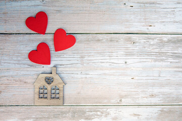 Wooden house with three red hearts on a wooden background. Love nest, love relationships. Buying a house with a young family. Affordable housing. banner. Family psychology, strong relations. 